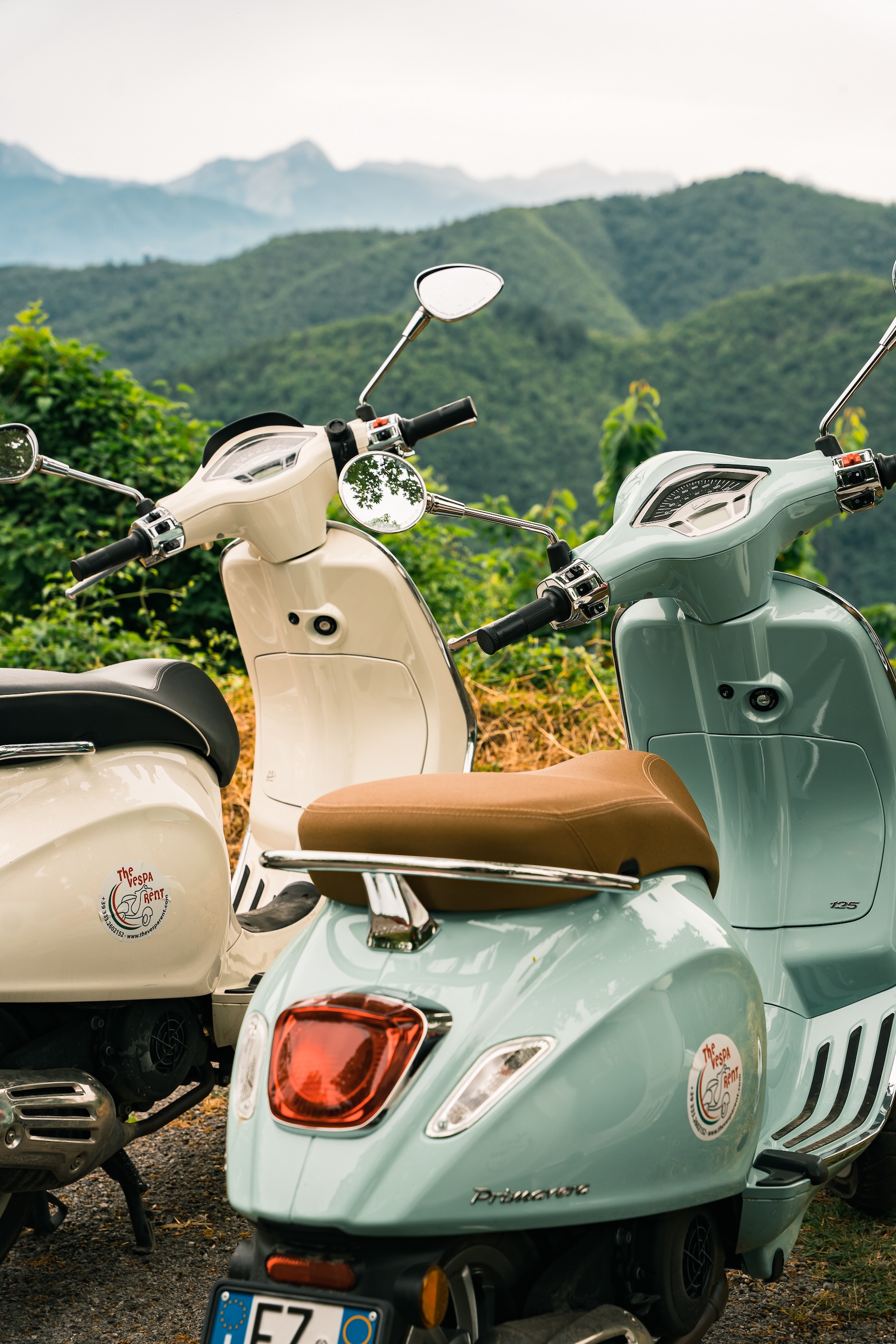 Two Vespas in front of green hills in Italy