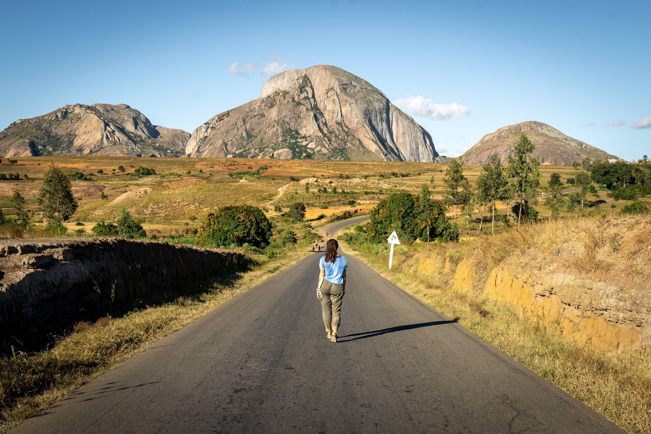 Femme qui marche sur une route qui mène aux montagnes